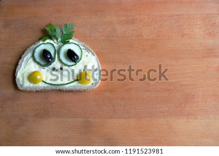 The funny creative little face on a butter sandwich consisting of tomato halves. cucumber. butter and parsley on the wooden board.Assemblage style