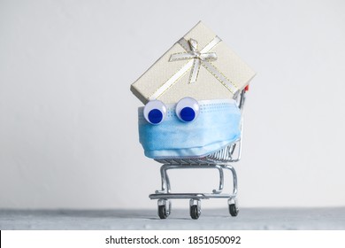 Funny Creative Shopping Cart With Protective Mask And Christmas Gift Box. Safety Christmas Shopping During Corona Virus Pandemic Concept.