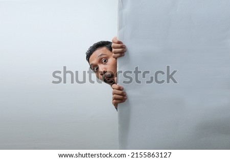 funny curious man peeking behind the wall