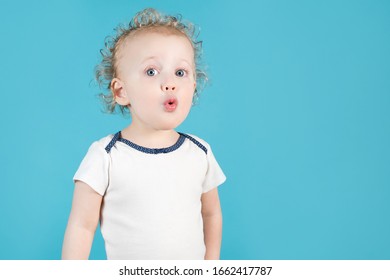 Funny Curly Baby Girl Of Two Years Makes A Surprised Face And Folds Lips With A Straw. Isolated On Blue