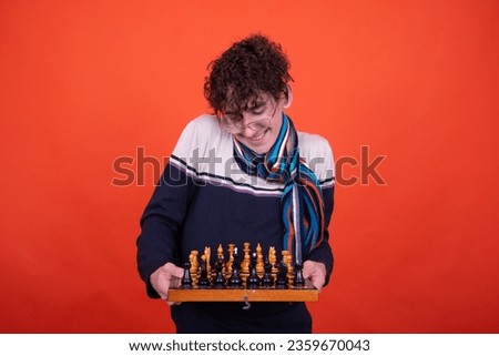 Funny curly guy posing in the studio against an orange background and playing chess.