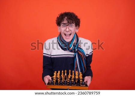 Funny curly guy posing in the studio against an orange background and playing chess.