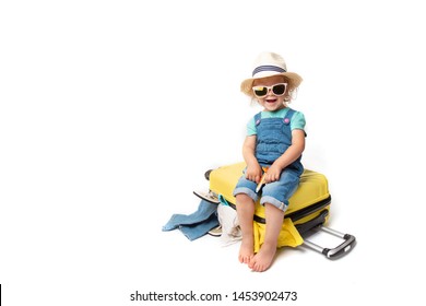 Funny Curly Little Baby Girl In A Hat, T-shirt And Jeans With A Yellow Suitcase Is Smiling  Isolated On White Background Waiting For An Airplane. Concept Trip With Kids