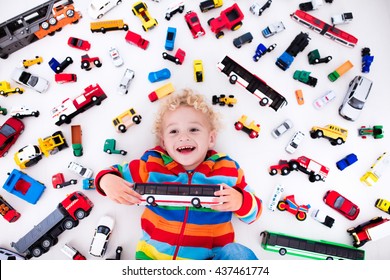 Funny Curly Toddler Boy Playing With His Model Car Collection Lying On The Floor. Transportation And Rescue Toys For Children. Toy Mess In Kids Room. View From Above. Many Cars For Little Boys.