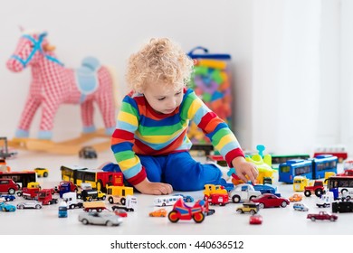 Funny curly toddler boy playing with his model car collection on the floor. Transportation and rescue toys for children. Toy mess in child room. Many cars for little boys. Educational games for kids.