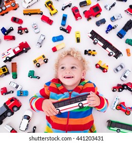 Funny Curly Toddler Boy Playing With His Model Car Collection Lying On The Floor. Transportation And Rescue Toys For Children. Toy Mess In Kids Room. View From Above. Many Cars For Little Boys.