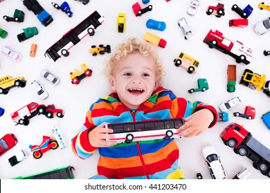 Funny curly toddler boy playing with his model car collection lying on the floor. Transportation and rescue toys for children. Toy mess in kids room. View from above. Many cars for little boys.