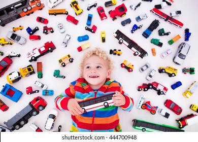 Funny Curly Toddler Boy Playing With His Model Car Collection Lying On The Floor. Transportation And Rescue Toys For Children. Toy Mess In Kids Room. View From Above. Many Cars For Little Boys.