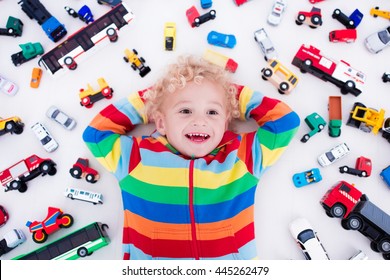 Funny Curly Toddler Boy Playing With His Model Car Collection Lying On The Floor. Transportation And Rescue Toys For Children. Toy Mess In Kids Room. View From Above. Many Cars For Little Boys.