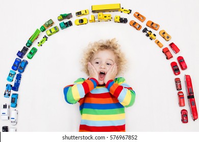 Funny Curly Toddler Boy Playing With His Model Car Collection On The Floor. Transportation And Rescue Toys For Children. Rainbow Toy Mess In Kids Room. View From Above. Many Cars For Little Boys