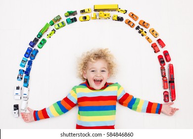 Funny Curly Toddler Boy Playing With His Model Car Collection On The Floor. Transportation And Rescue Toys For Children. Rainbow Toy Mess In Kids Room. View From Above. Many Cars For Little Boys.