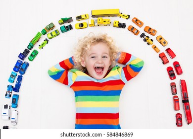 Funny Curly Toddler Boy Playing With His Model Car Collection On The Floor. Transportation And Rescue Toys For Children. Rainbow Toy Mess In Kids Room. View From Above. Many Cars For Little Boys.