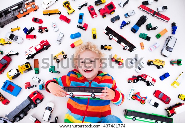 Funny curly toddler boy playing with his model car\
collection lying on the floor. Transportation and rescue toys for\
children. Toy mess in kids room. View from above. Many cars for\
little boys.