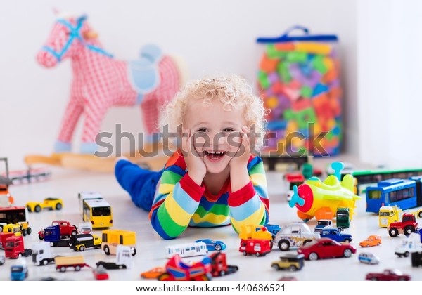 Funny curly toddler boy playing with his model car\
collection on the floor. Transportation and rescue toys for\
children. Toy mess in child room. Many cars for little boys.\
Educational games for\
kids.