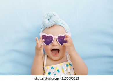 Funny cute baby girl on summer vacation. Child having fun in swimming pool. Sweet toddler girl in colorful swimsuit and sunglasses relaxing on sunbed.