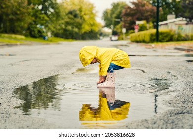 A Funny cute baby girl wearing yellow waterproof coat and boots playing in the rain - Powered by Shutterstock