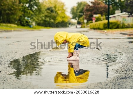 A Funny cute baby girl wearing yellow waterproof coat and boots playing in the rain