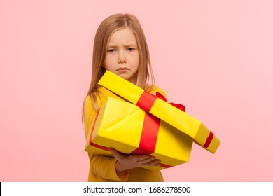 Funny Cute Child Unhappy With Bad Birthday Present. Portrait Of Sad Little Girl Opening Gift Box And Looking At Camera With Dissatisfied Expression. Indoor Studio Shot Isolated On Pink Background