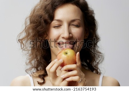 Funny cute curly beautiful woman in basic white t-shirt enjoy licks fresh apple healthy food posing isolated on over white background. Natural Eco-friendly products concept. Copy space