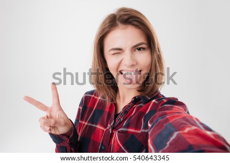 Funny cute girl winking and showing tongue while taking selfie isolated on a white background