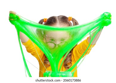 Funny Cute Little Girl Stretching Green Slime With Her Hands And Looking Through It On White Background. Making Colorful Slime. Kids Hands Playing Slime Toy.