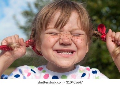 A funny cute outdoor close up portrait of a little girl presenting Pippi Longstocking with her eyes closed and making faces  