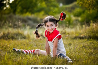 A funny cute outdoor portrait of a little girl presenting Pippi Longstocking and showing out out her tongue. 