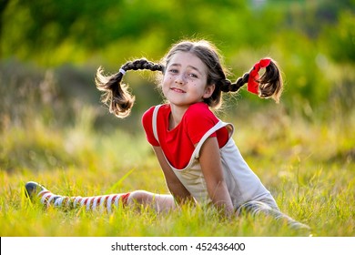 A funny cute outdoor portrait of a little girl presenting Pippi Longstocking and showing out out her tongue.