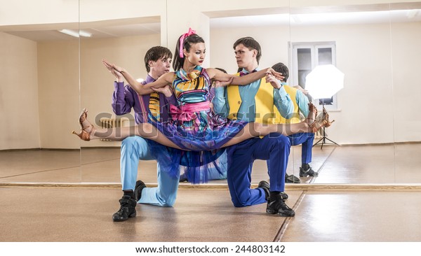 Funny dancer three people Two man one woman\
dressed in boogie-woogie rock\'n\'roll pin up style posing together\
in studio against mirror reflection Girl sit on splits on gays \
knees Colorful costumes