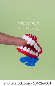 a funny denture biting the forefinger of a young man and the text happy april fools day, on a green background