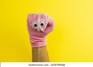 funny doll  sock with googly eyes on a yellow background, hand theater