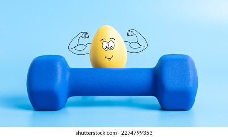 Funny Easter egg with cute face shows his muscles behind dumbbell on blue background. Strong athlete yellow egg character in theme of sports, training and healthy lifestyle. Protein and nutrition