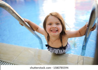 Funny Emotional Girl Child In A Striped Swimsuit Plays By The Pool. Concept Summer Vacation With Children And Child Safety. Child Alone Near Outdoor Pool