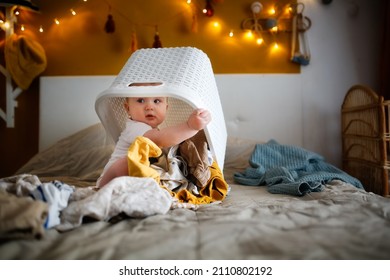 funny european chubby kid playing with laundry basket on bed in cozy bedroom, mom help and home routines, motherhood and baby care