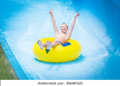 Funny excited child enjoying summer vacation in water park riding yellow float laughing.