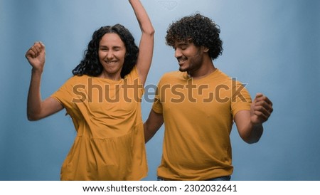 Funny excited happy couple Hispanic woman Latino wife girlfriend dance with carefree Indian man active cheerful husband boyfriend dancing having fun celebrate fooling around at blue studio background