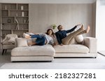 Funny excited millennial spouses of new homeowners falling on big soft couch at home. Young couple celebrating moving into first common house. Real estate, renovation, furniture for hoe concept