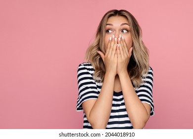 Funny Excited Young Woman Covering Open Mouth Looking Aside To Copy Space. Surprised Shocked Happy Blond Female In Excitement And Positive Shock Emotion Face Expression Isolated Over Pink Studio Wall