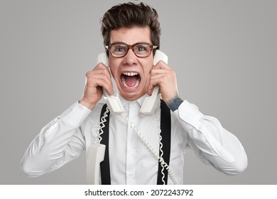 Funny Exhausted Male Operator Shouting While Speaking On Telephone On Gray Background In Studio And Looking At Camera