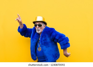 Funny and extravagant senior man posing on colored background - Youthful old man in the sixties having fun and partying