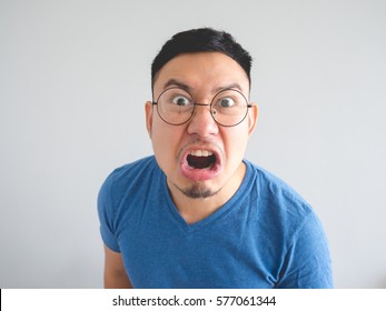 Funny face of angry Asian man with blue t-shirt and eyeglasses.