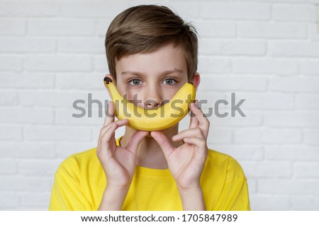 Funny face with banana. Comic boy. Young boy in yellow t-shirt holding banana with a smile. Funny expressions. Banana like smile.  Food concept.  Fresh banana. Yellow style