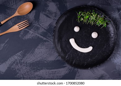 Funny Face Drawn With White Sauce And Microgreen On The Black Ceramic Plate. Top View. Ecological Eating Concept