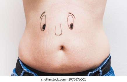 A funny face painted on the belly of an unrecognizable fat man. The eyes and nose are painted, and the mouth is the navel. - Shutterstock ID 1978876001