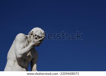 Funny face palming statue background with copy space. Concept for frustration, failure, annoyance. Statue labelled Cain coming from killing his brother Abel (Tuileries Garden, Paris, France)