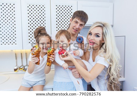 Funny family of four on the background of bright kitchen beautiful have fun fooling around eating donuts. The concept of family happiness. The full family.