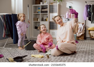 Funny Family Having Fun While Doing Housework And Cleaning. Smiling Woman Taking Selfie With Daughters. Happy Girl Uses Smartphone To Talk Video Shows Kids Helping Her Clean Bathroom.