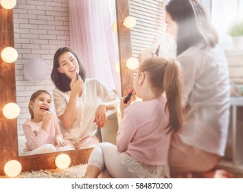 Funny Family At Home. Mother And Her Child Girl Are Doing Your Makeup And Having Fun Near Mirror. Mom And Daughter Wear Lipstick In Kids Room.