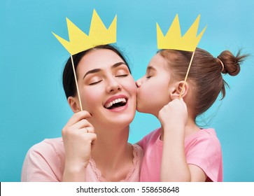 Funny family on a background of bright blue wall. Mother and her daughter girl with a paper accessories. Mom and child are holding paper crown on stick.