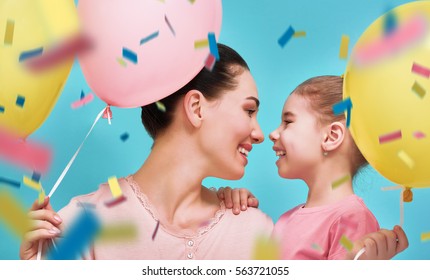 Funny Family On A Background Of Bright Blue Wall. Mother And Her Daughter Girl Are Having Fun With Balloons And Confetti. Yellow, Pink And Turquoise Colors.